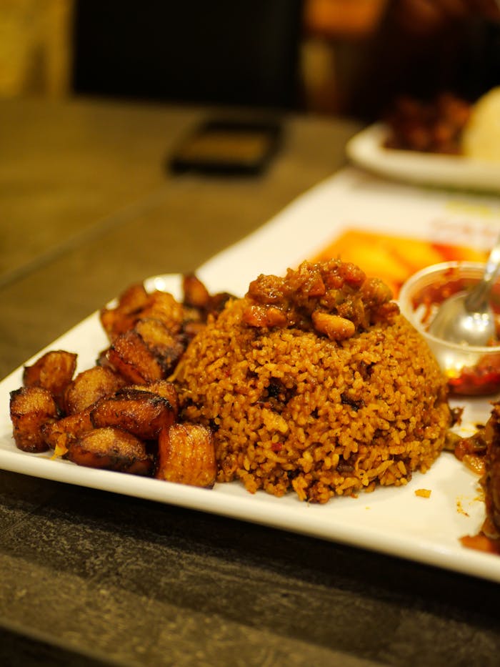 Close-up of Jollof rice with fried plantains and sauce on a plate, perfect for food enthusiasts.