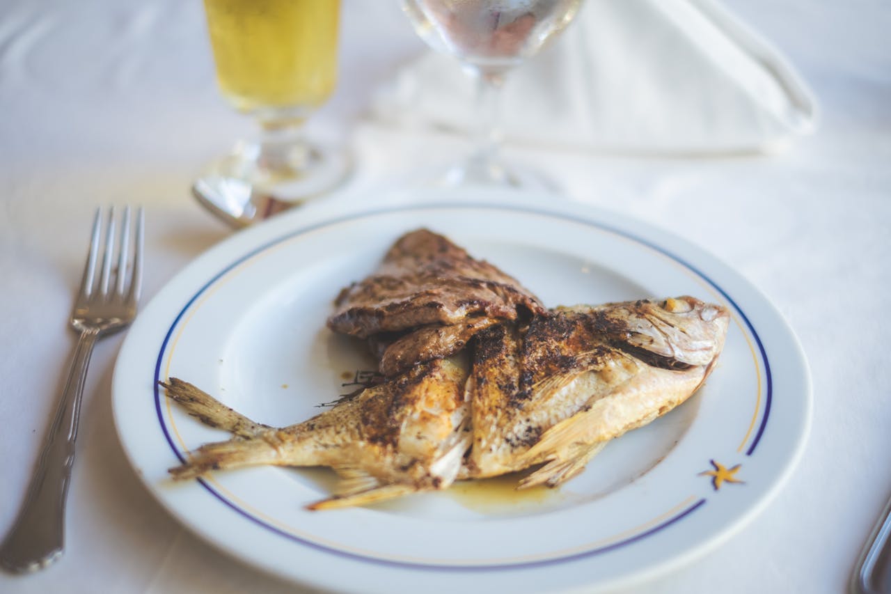 Close-up of a delicious grilled fish served on a white plate with a fork and glass of wine.